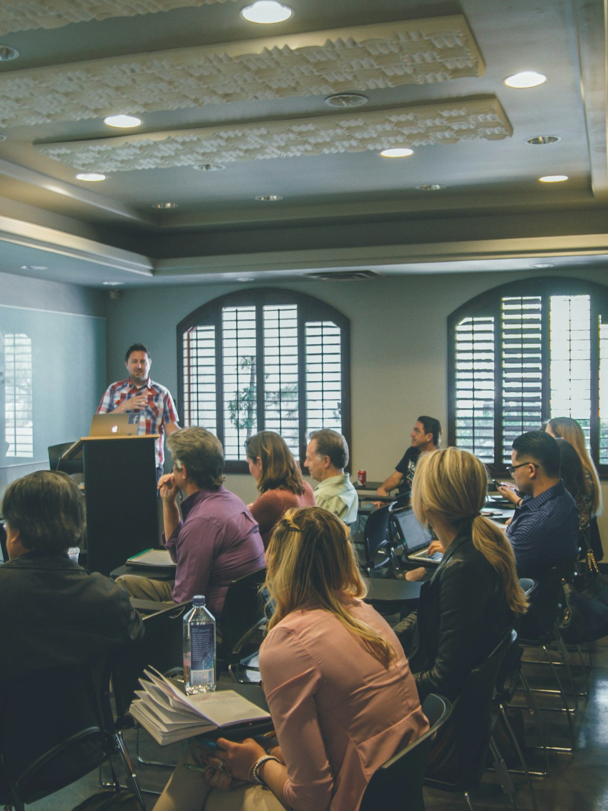 A speaker addressing a seated group in a training room.