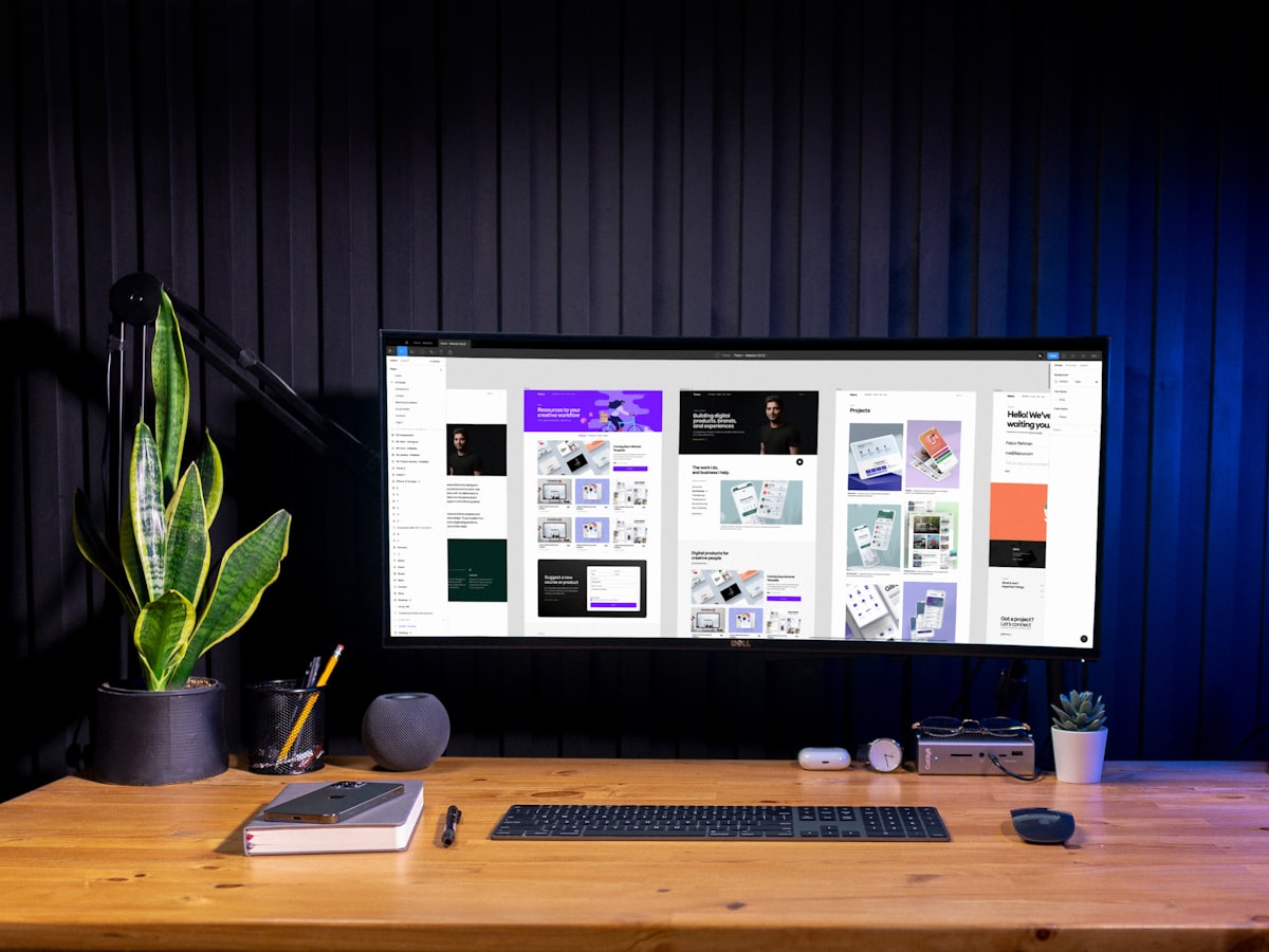 An ultrawide monitor on a studio desk showing a design tool full of layout artboards.