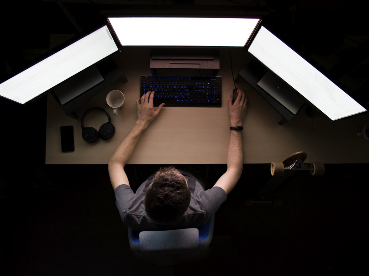 Overhead view of an editor working at a three-screen workstation in a darkened room.